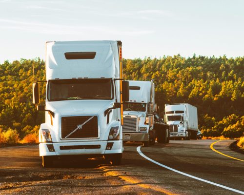 Three semi trucks driving on a highway through a forested landscape in Arizona.